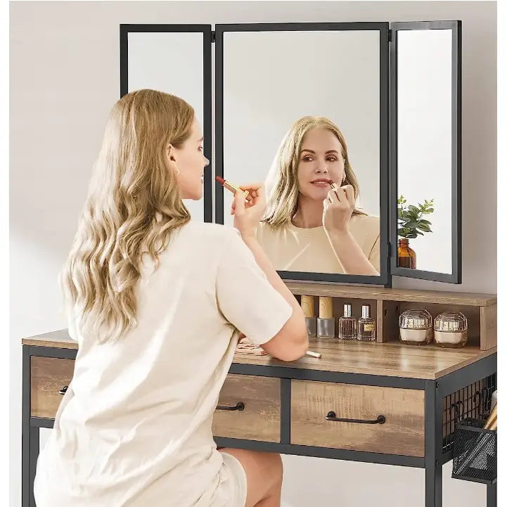 Loftsminkebord i tre og sort metall med treveis speil, kvinne sminker seg, små flasker på bordet.