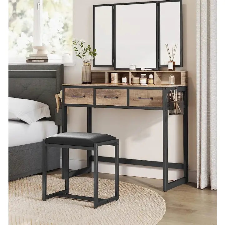 Loftsminkebord med krakk, skråvisning som viser svart metallramme, trefargede skuffer og tredelt speil i lyst rom.