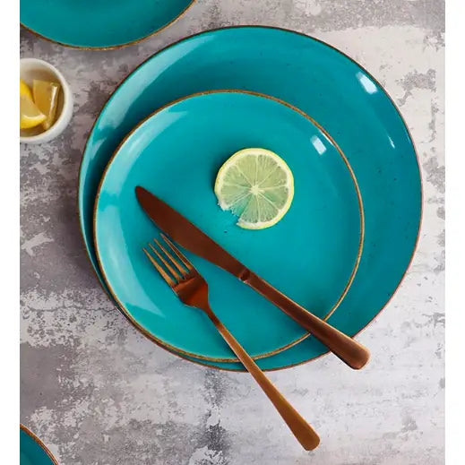 To blå Lubiana Boss keramiktallerkener med brune kanter, sitronskive og gullbestikk sett ovenfra.