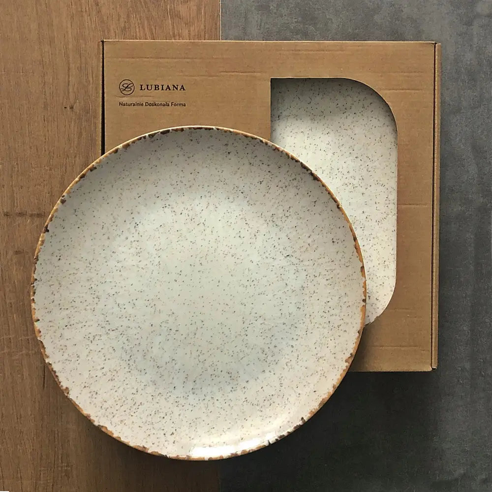 Middagstallerken i beige porselen med brunspettede detaljer og mørk kant, plassert på eske.