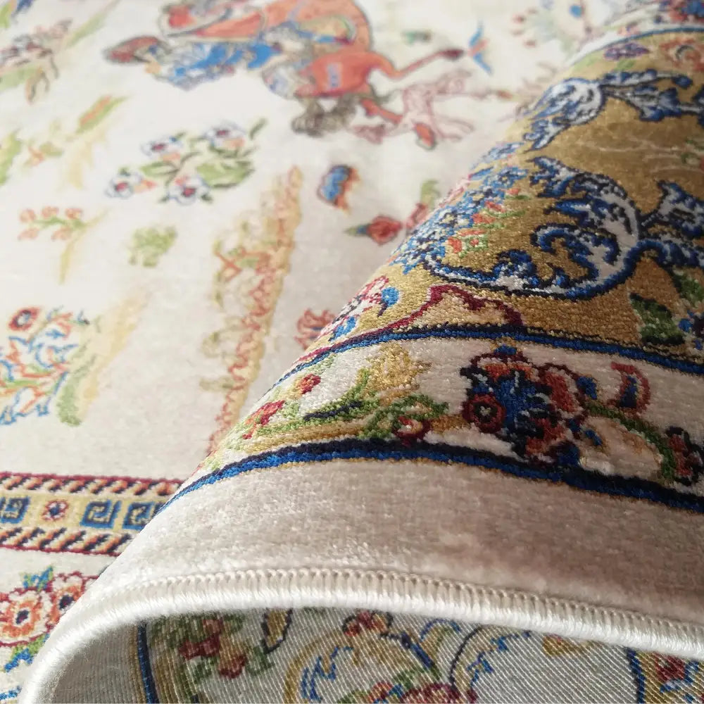 Qum Silk kremet teppe 160x230, nærbilde av kant, tykkelse og intrikate blå, røde og gyldne mønstre.