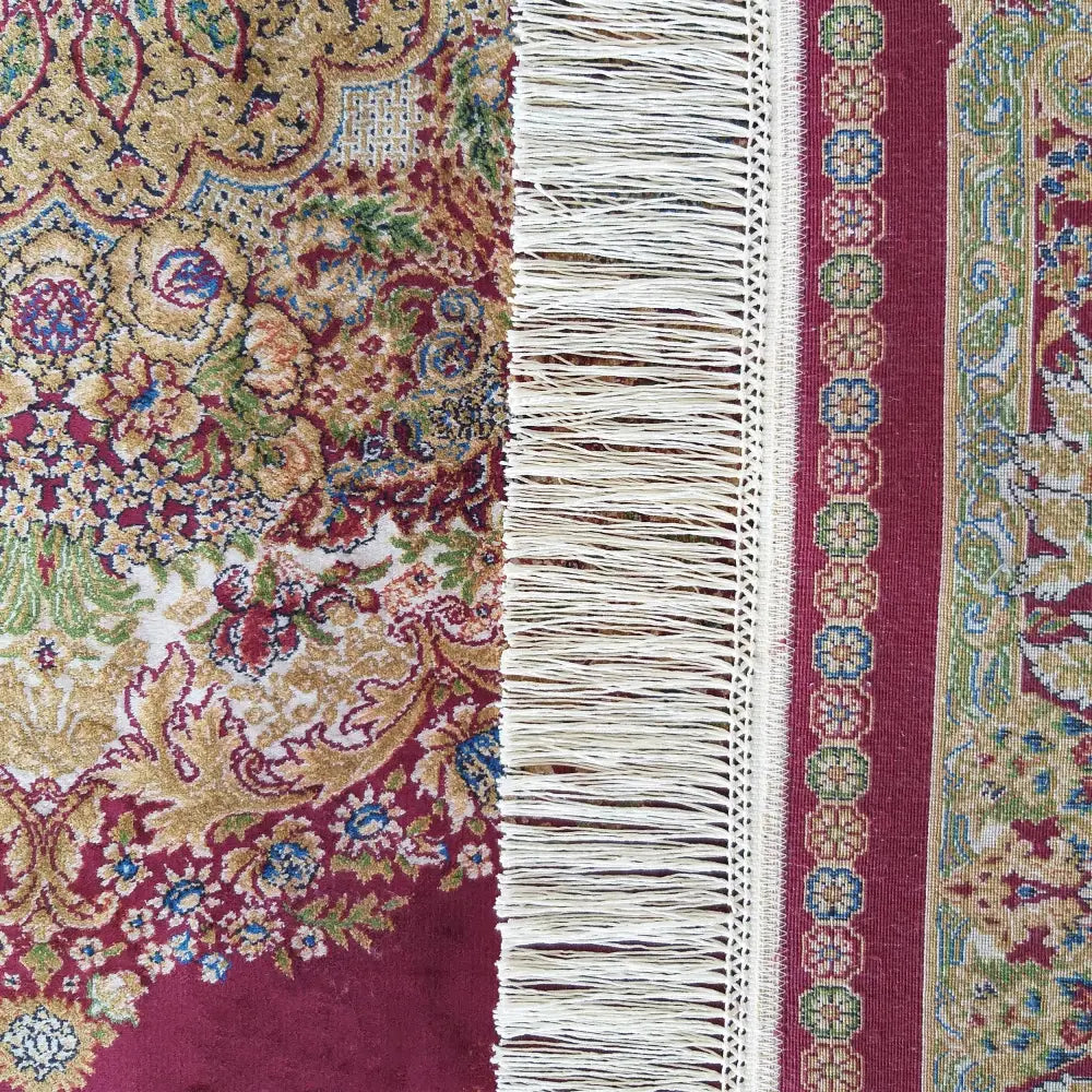 Qum Silk Tepe 01, nærbilde av rødt teppe med intrikate gull- og blåmønstre og kremfargede frynser langs kanten.