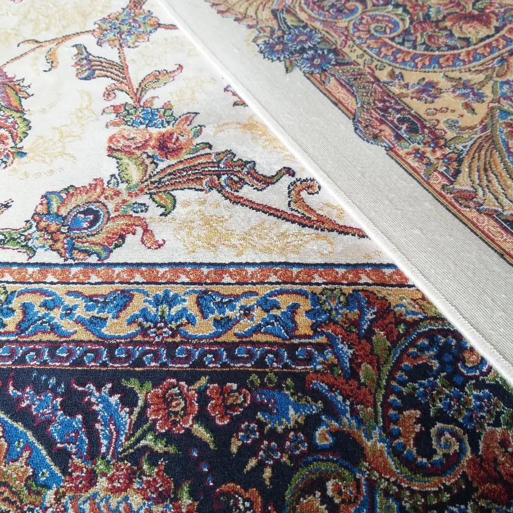 Qum Silk Tepe, nærbilde av kremhvitt teppe med orientalsk mønster, blå og rustrøde blomster og detaljerte border.