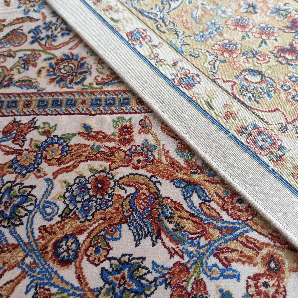 Qum Silk Tepe, nærbilde av kremfarget teppe med orientalsk mønster, fugler, blomster og dekorative kanter.