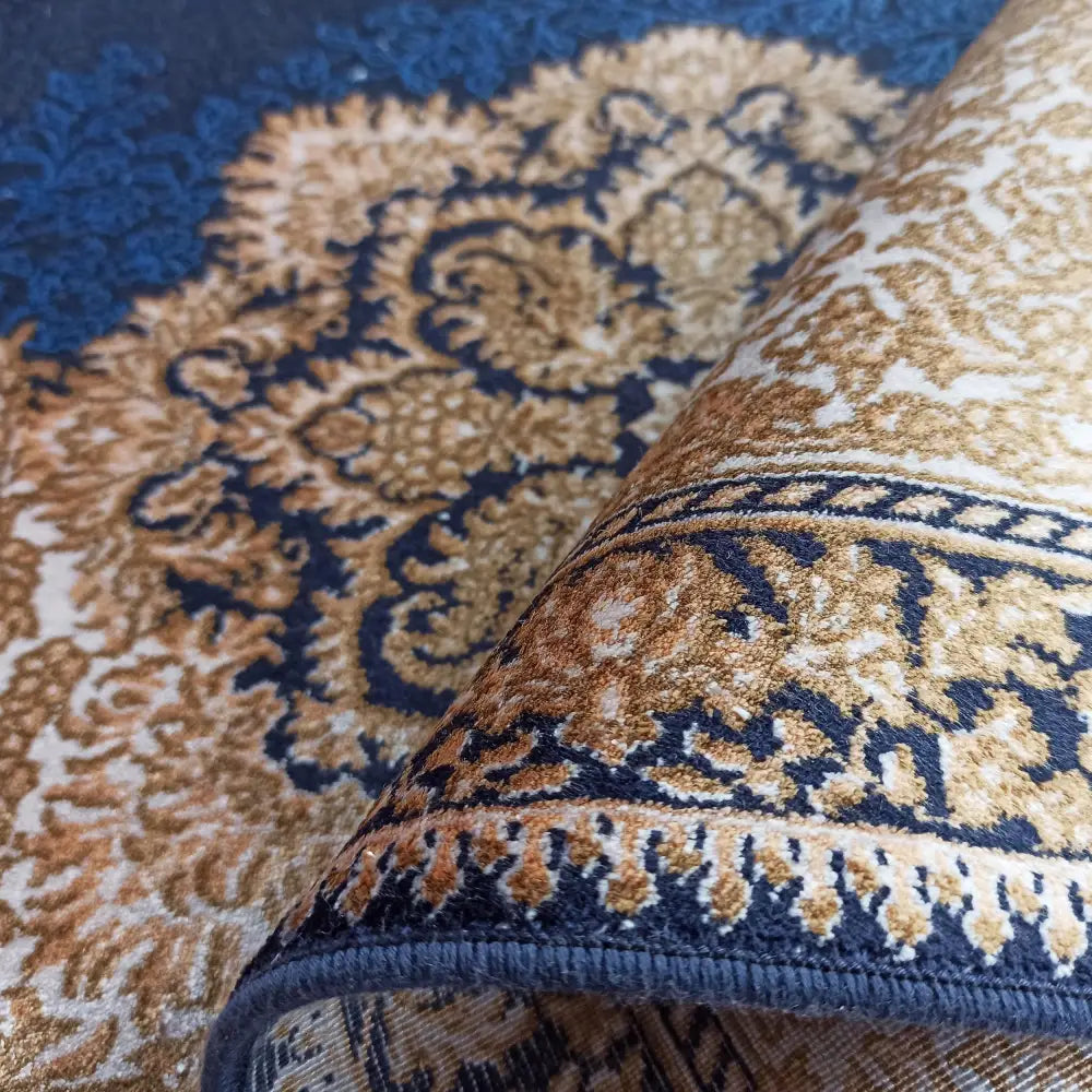 Qum Silk Tepelig Navy, nærbilde av teppets marineblå og gullmønstrede hjørne med synlig silkestruktur.