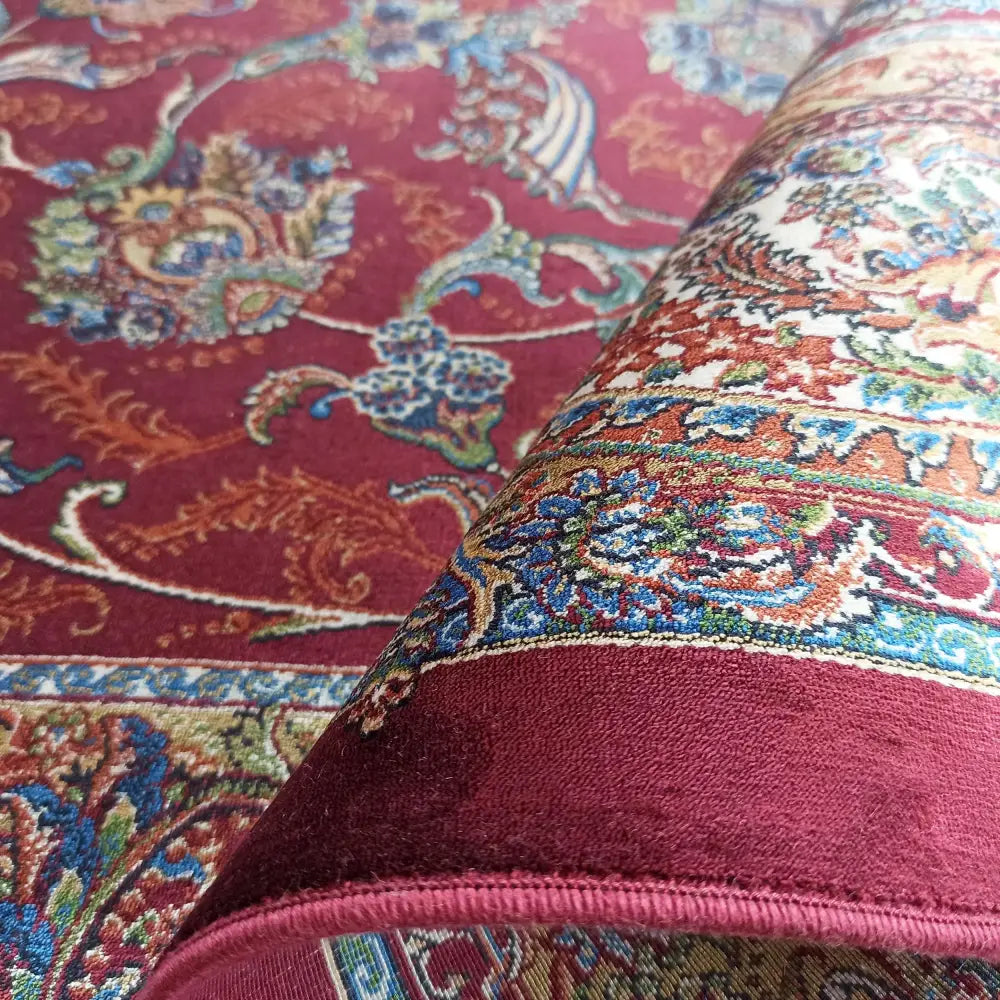 Qum Silk tepematte i burgunder, nærbilde av blomstermønster og bladverk, delvis rullet opp.