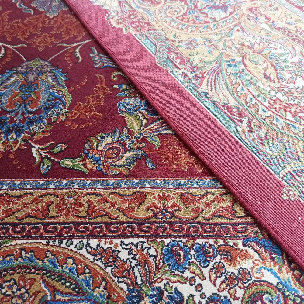 Qum Silk teppe i rødt, nærbilde av blå, grønne og gullfargede blomster og solid rød kant.