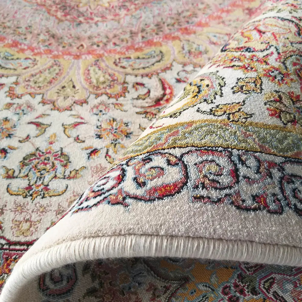 Luksuriøst kremfarget teppe, nærbilde av bøyd hjørne med orientalske blomstermønstre i pastellfarger.