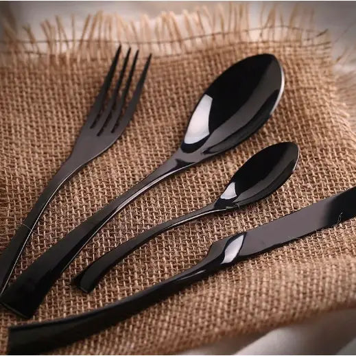 Luksuriøst Kaja bestikksett i svart, fire deler pent arrangert på grovt brunt striestoff.