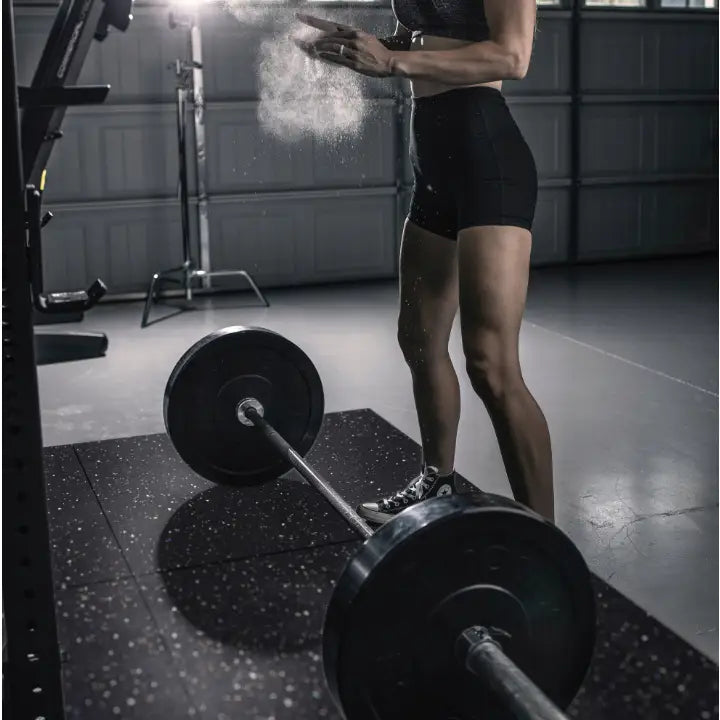 Lyddempende matte for tredemølle 180x80, kvinne gjør klar til styrketrening med kalkstøv over vektstang.