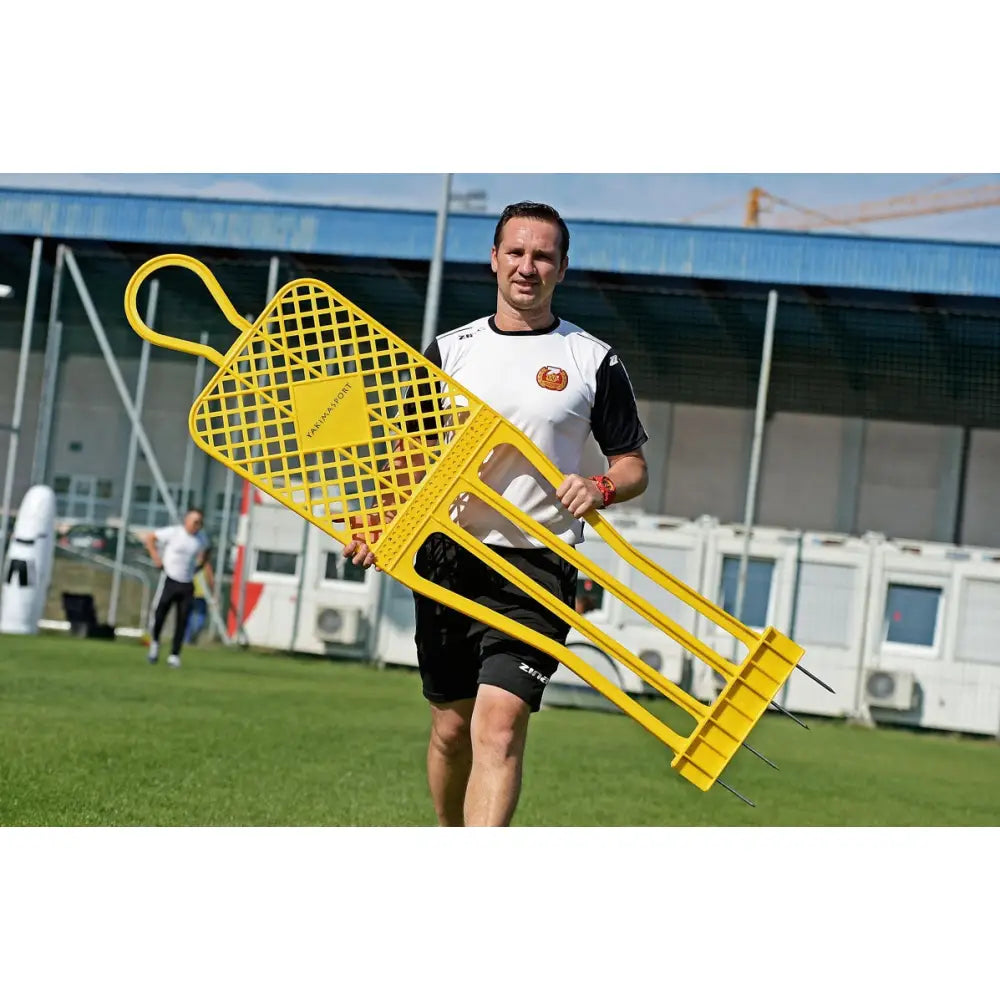 Mål Fodboldnett ELITE 180 cm Rød, vist utendørs mens en mann bærer gul treningsfigur med netting og metallpigger.