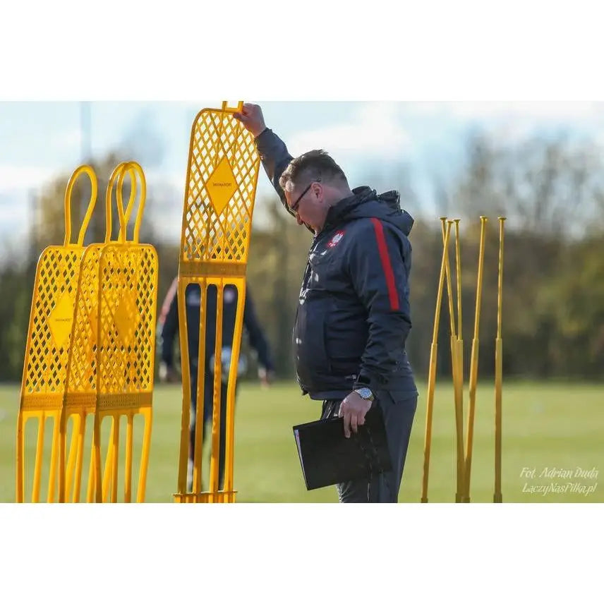 Gule treningsmannequiner i plast på gressbane, person i treningsklær holder én mannequin fra siden.