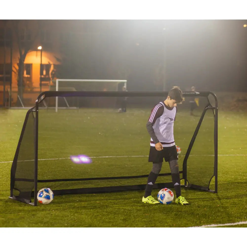 Svart fotballmål GIZA ŻAK 3x1,55m i metall med nett, sett skrått, ung spiller og to baller på opplyst gressbane om kvelden.