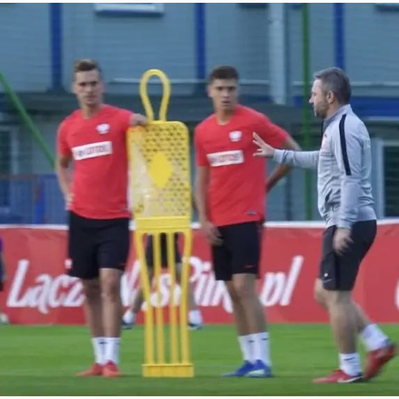 Målmuren ELITE 180 cm gul, plastfigur på fotballbane med to spillere og trener i rød trøye under instruksjon.