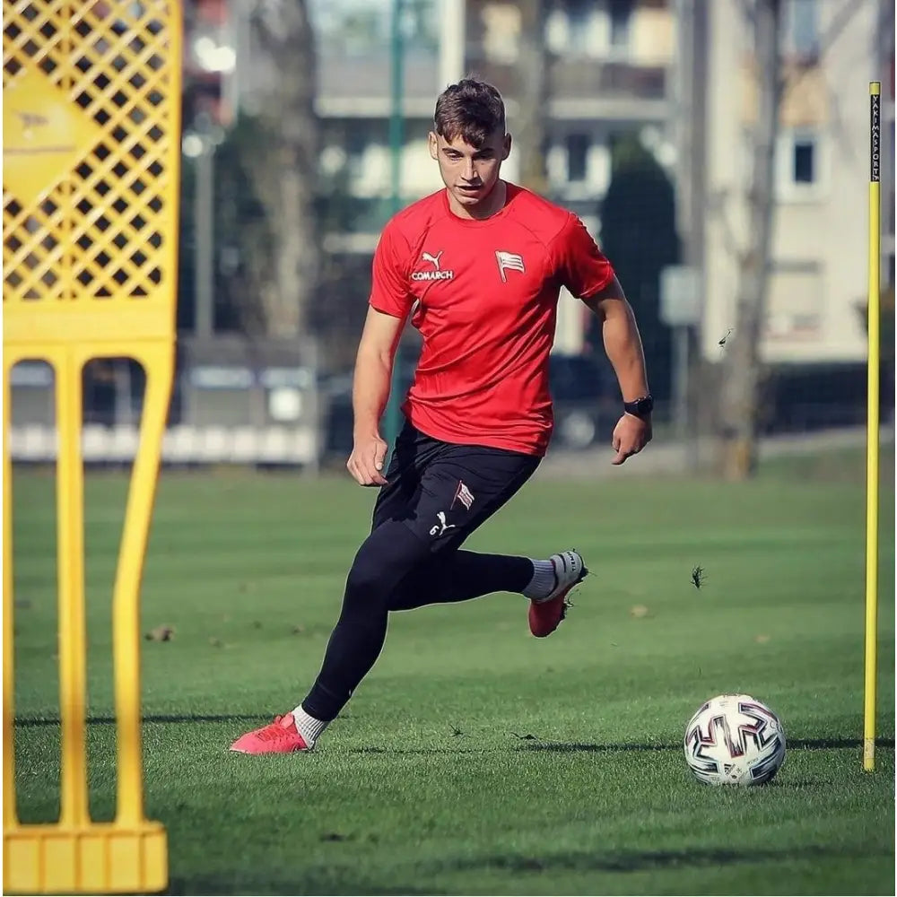 Målmuren ELITE 180 cm Gul brukt til fotballtrening, med markører foran og spiller i aksjon på gress.