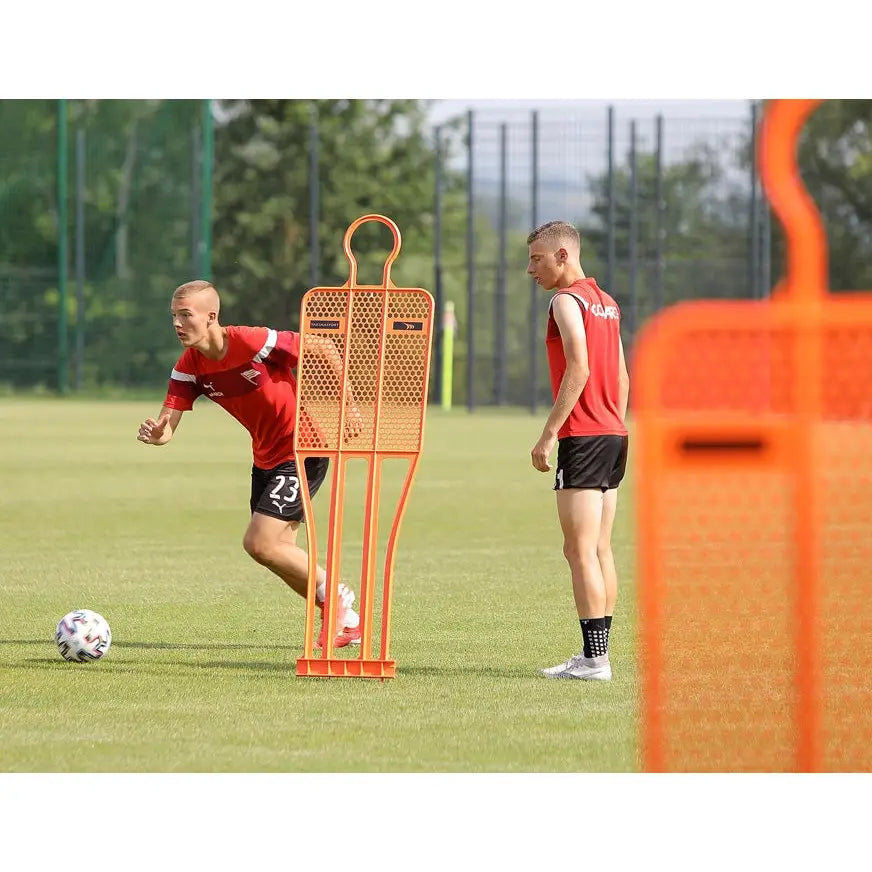 Målstolpe PRO 180 cm i nylon brukes som oransje markør under fotballtrening på gressbane med to spillere.