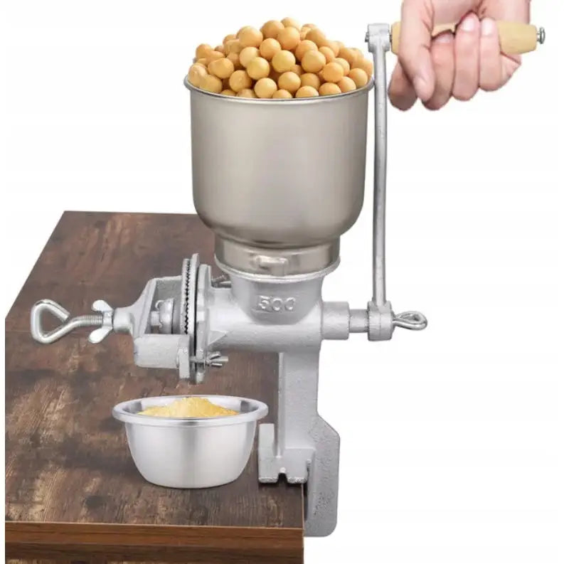 Manuell kornkvern i metall, festet til bordkant, bønner fylles på og malt korn samles i skål under.