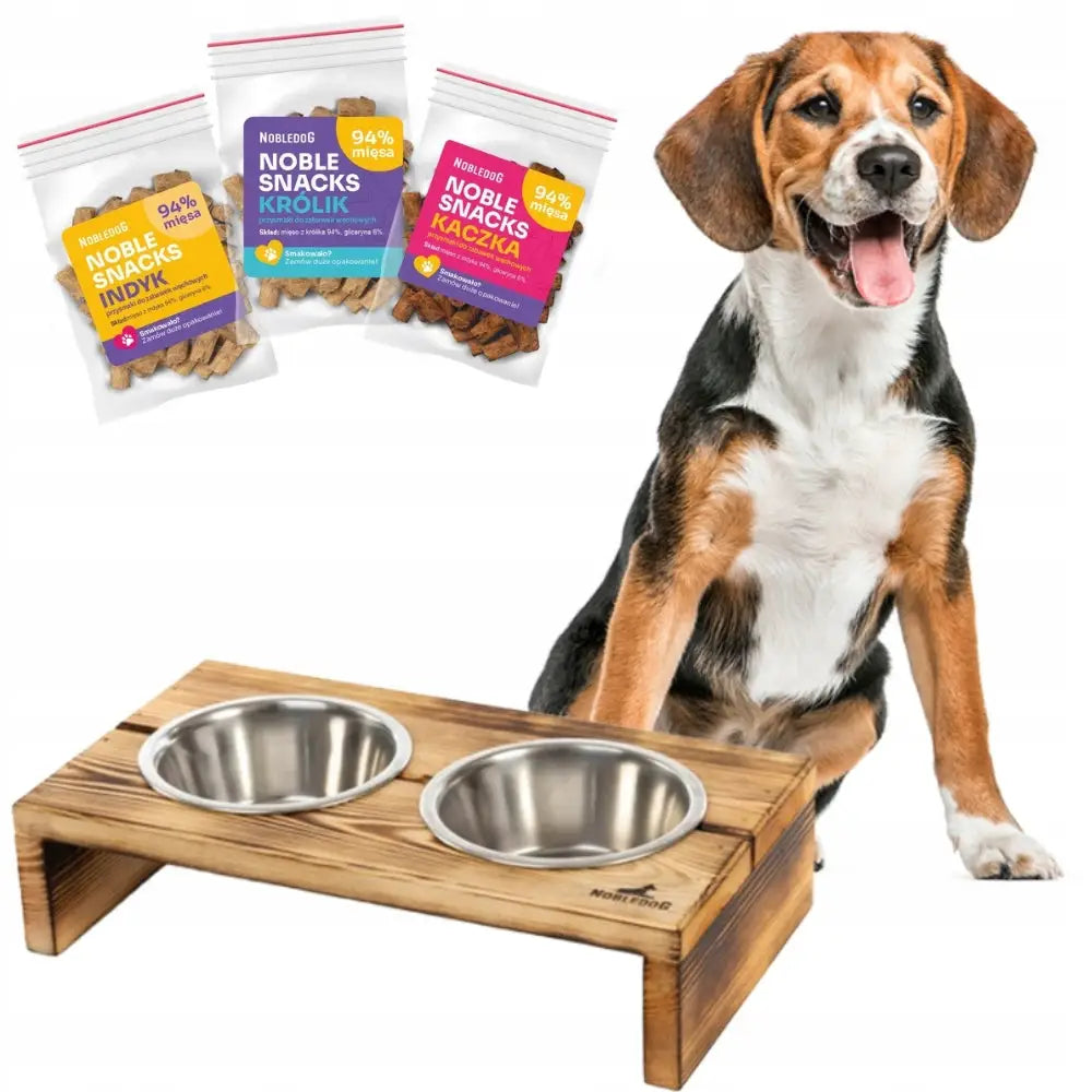 Matstativ i lyst tre med to matskåler i stål, mellomstor hund og snacksposer synlige i bakgrunnen.