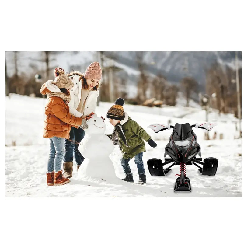 Metall akebrett skisleder Monzana, sort og rød kjelke sett forfra på snø foran fjell og barn som lager snømann.