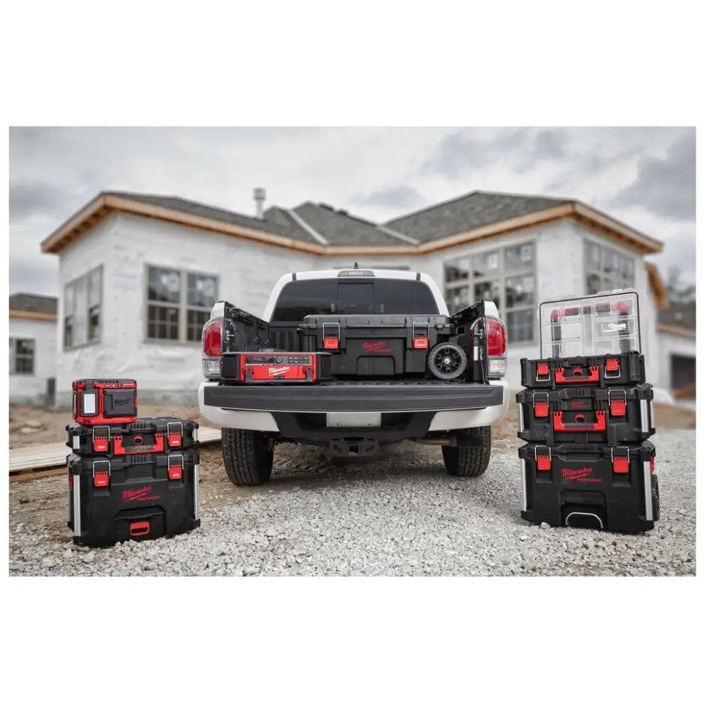 Milwaukee Packout kasse på hjul, stablet med flere bokser bak pickup på byggeplass, viser håndtak og hjul.