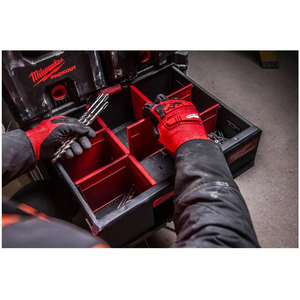 Milwaukee Packout verktøykasse, sett ovenfra mens en person med røde hansker sorterer metallbor i flere rom.