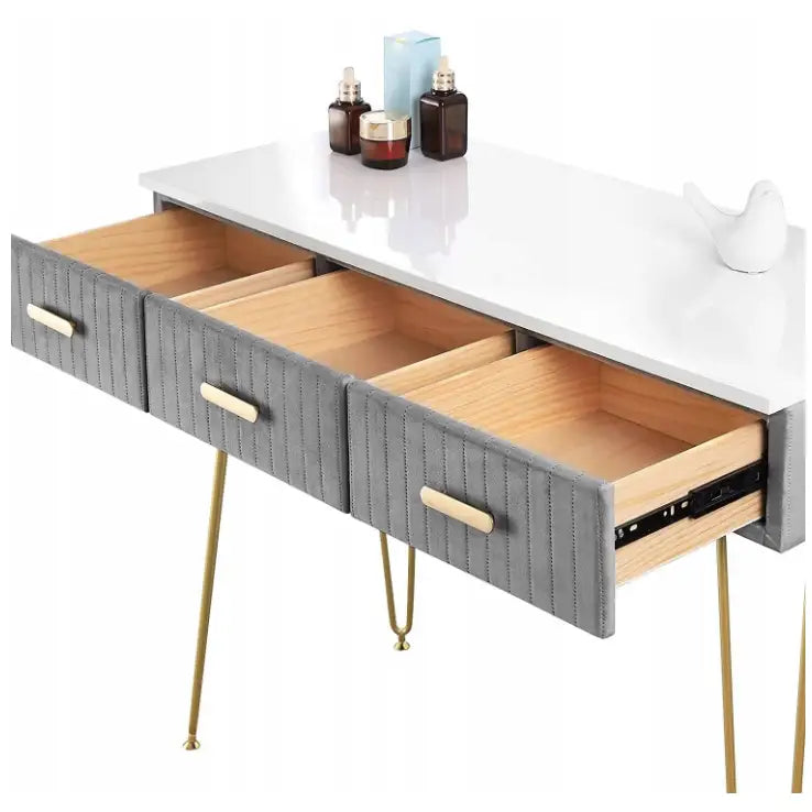 Moderne sminkebord med hvit topp, tre grå skuffer, gylne ben og dekor, sett fra skrå vinkel på soverom.