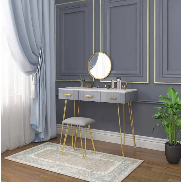 Moderne grått sminkebord med gullhåndtak, rund speil med gullramme og polstret krakk på lyst teppe.