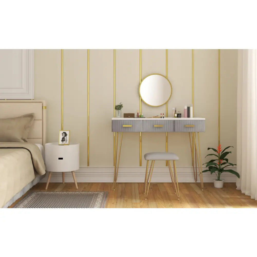 Moderne sminkebord i grått med tre skuffer, gullben, krakk og rundt speil, plassert mot beige vegg.