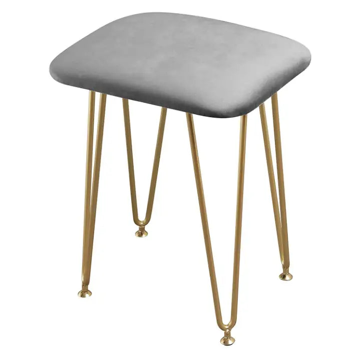 Grå krakk med mykt sete og slanke gullben, vist fra skrå vinkel mot toppen på lyst gulv.