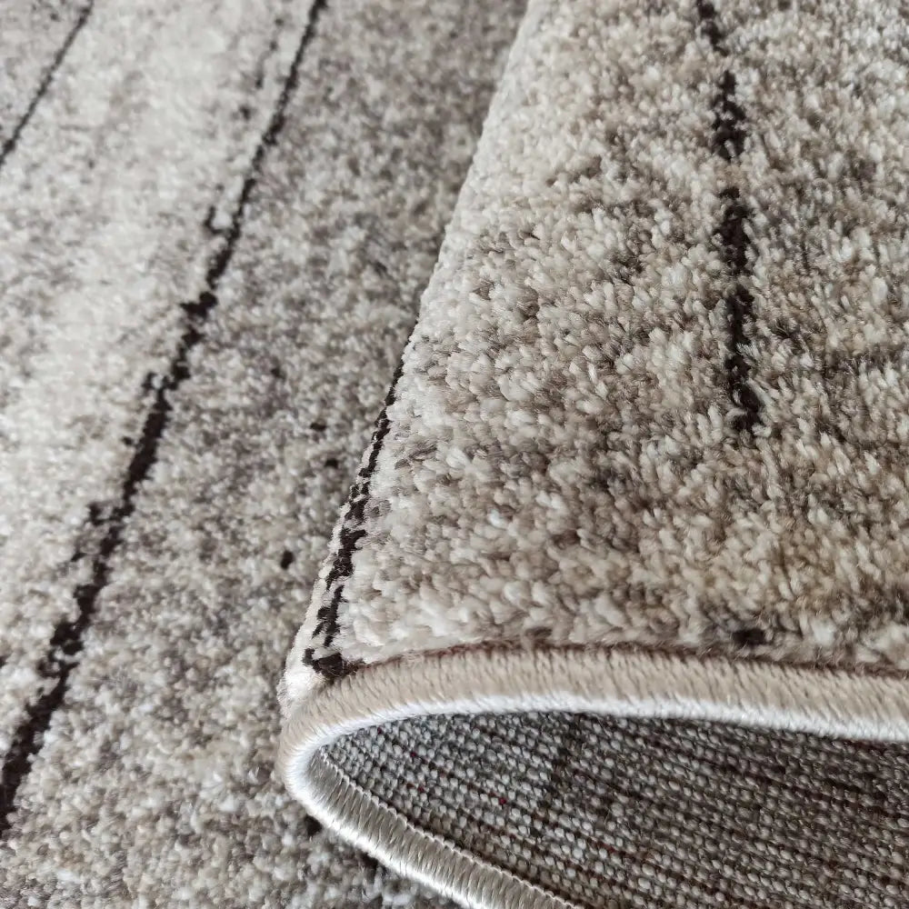 Moderne teppe Panamero 20, nærbilde av grå og beige tekstur, oppbrettet kant viser tykkelse og bakside.