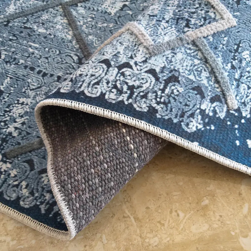 Moderne Tepe Hypnotik-teppe, detaljert hjørne med blått og grått mønster, synlig søm og grå vevd bakside.