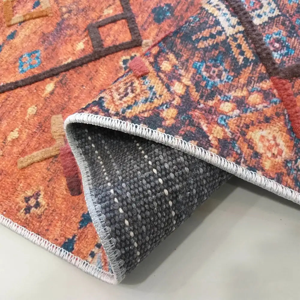 Moderne teppe med orientalsk mønster i oransje og blått, nærbilde av tekstur, brettet hjørne og hvit kant.