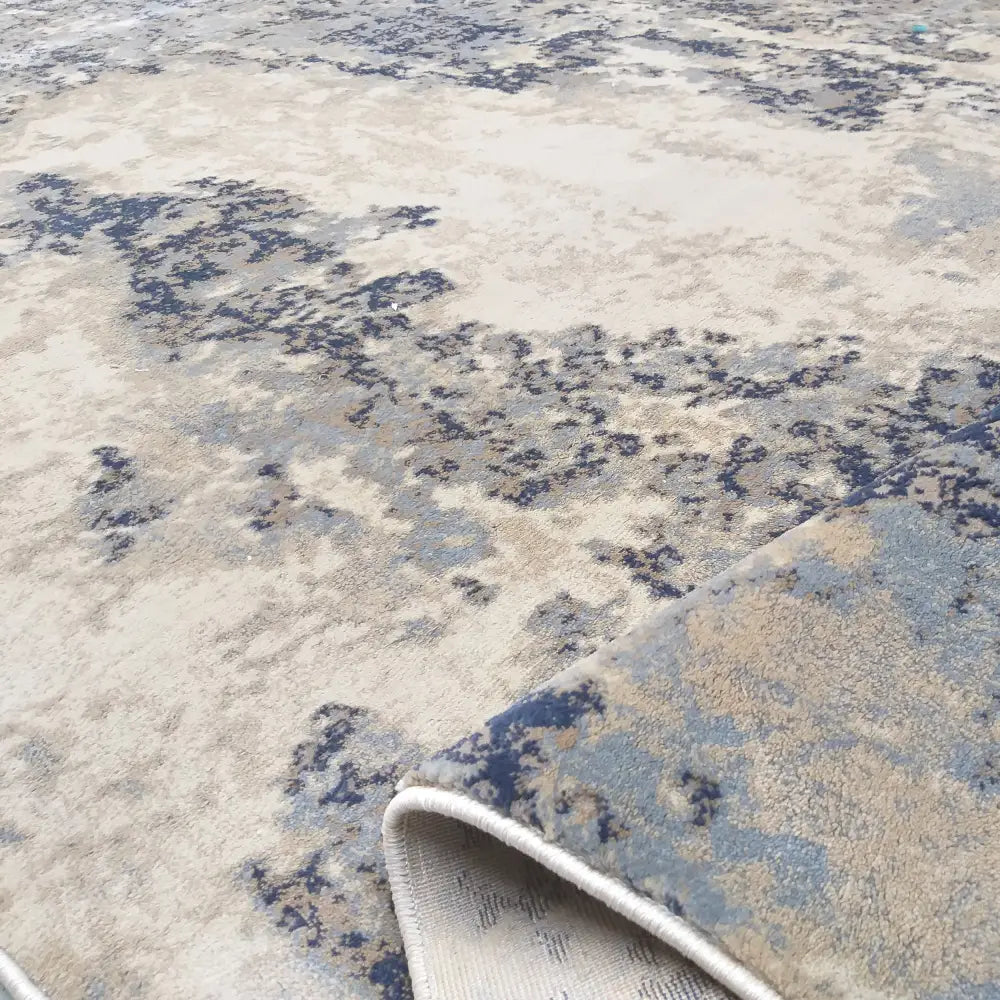 Moderne Tepe Milas teppe, nærbilde av brettet hjørne som viser tettvevd blått, beige og grått abstrakt mønster.