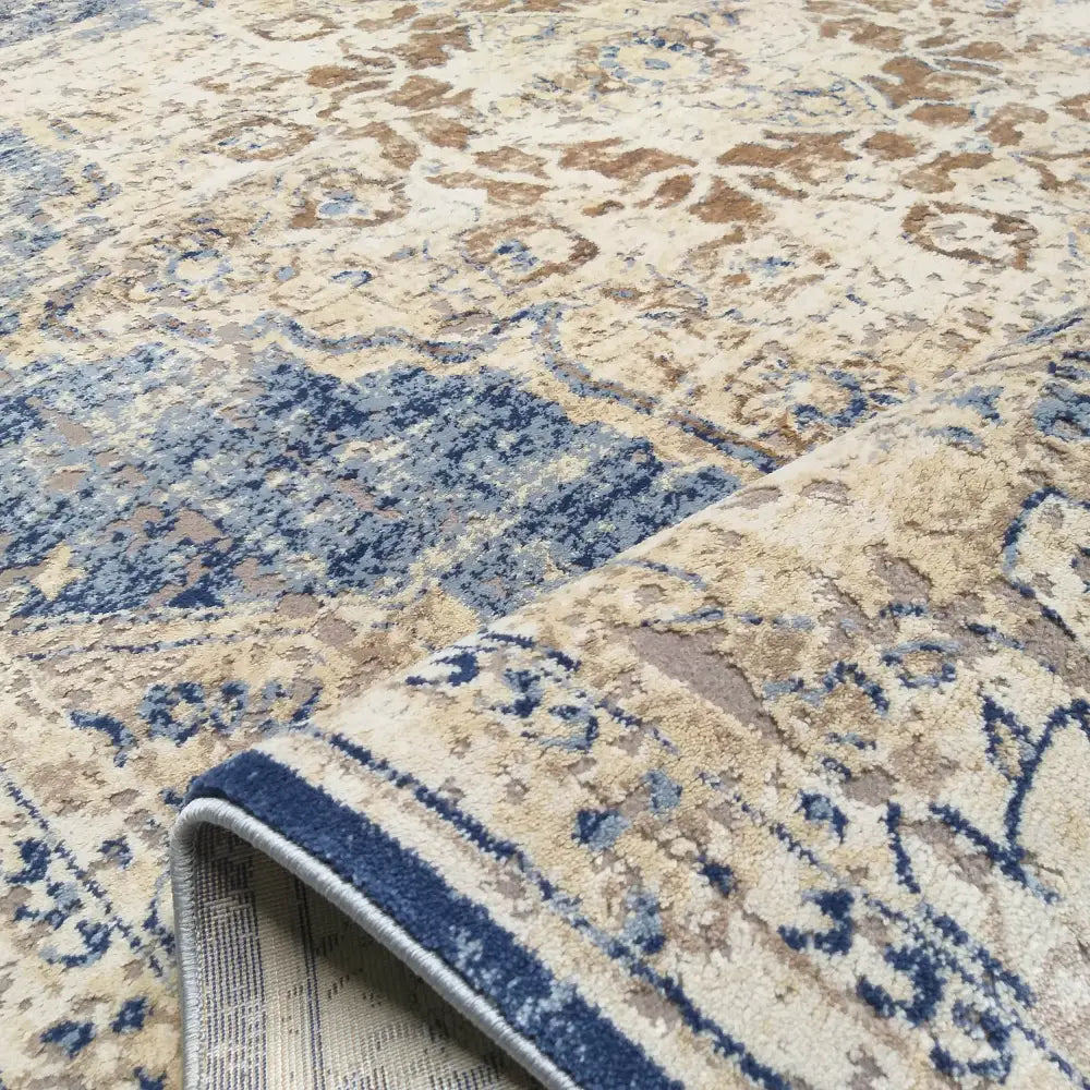 Tepe Milas Soft Shrink teppe, nærbilde av blått og beige mønster med oppbrettet hjørne som viser tekstur.