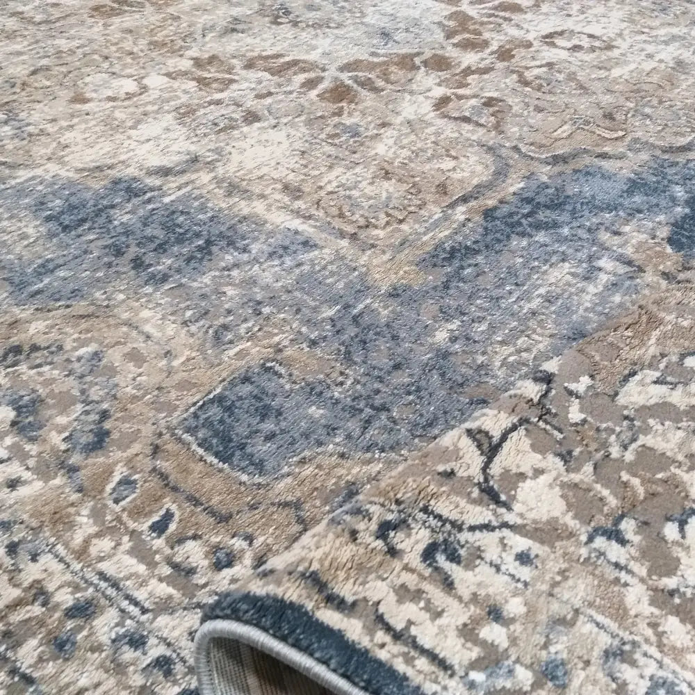 Tepe Milas Soft Shrink teppe, nærbilde av blått og beige mønster med oppbrettet hjørne som viser tekstur.