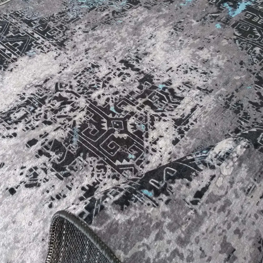 Moderne tepedesign EFES 100, nærbilde av grått teppe med oppbrettet hjørne og abstrakt etnisk mønster.