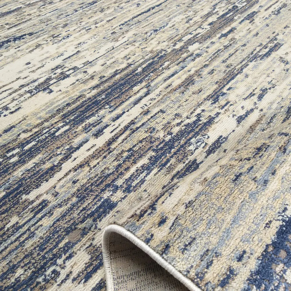 Moderne teppematte Milas Soft Shrink i blått, beige og grått, nærbilde med brettet hjørne som viser baksiden.