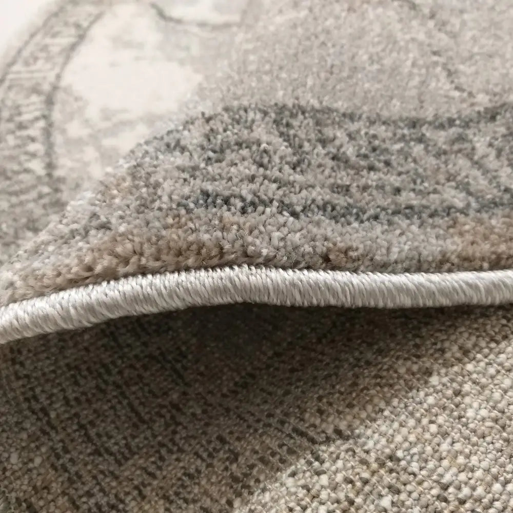 Moderne Vista 04 grå rundt teppe, nærbilde av brettet hjørne med lys kant og tettvevd beige-grå tekstur.