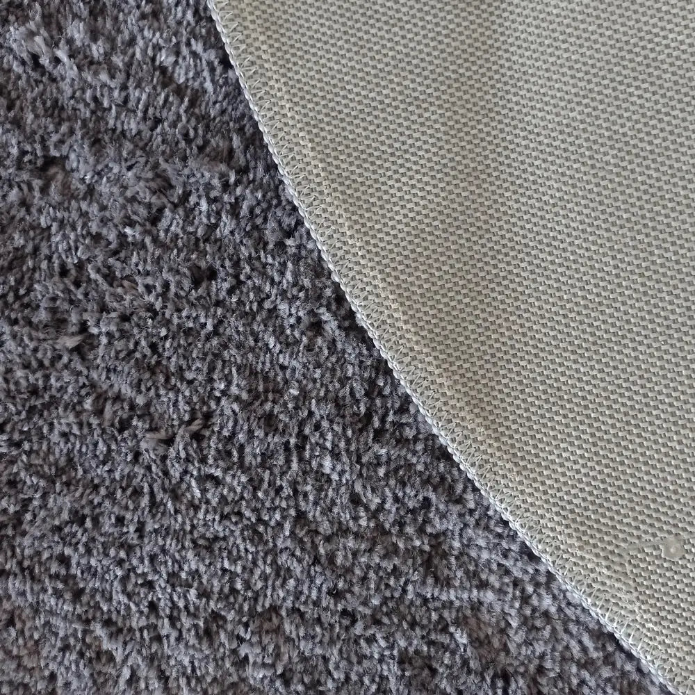 Mørk stålblå Kamel RundTepe, detalj av beige vevd kant og tydelig søm mot myk, mørkegrå overflate.