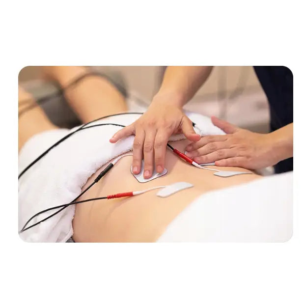 Muskelstimulator med fire elektrodepads på mage, person tilpasser plassering av padene med hendene.