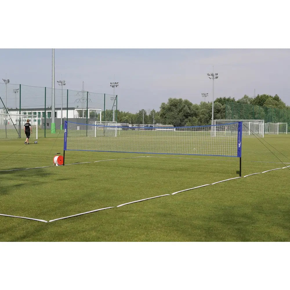 Naturlig gressmatte sett med blå stolper og hvitt nett, markeringstau på grønn gressbane, sideperspektiv.