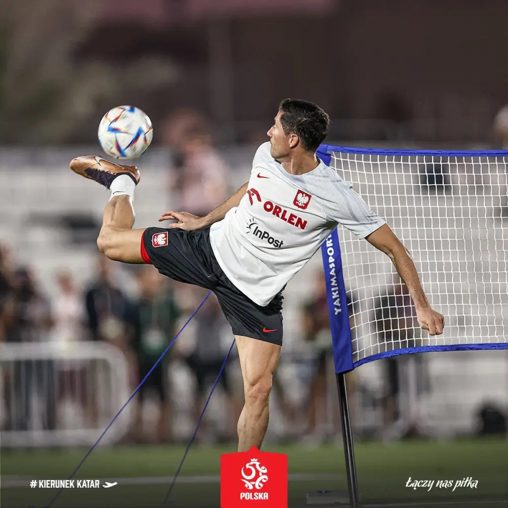 Naturlig gressmatte sett, fotballspiller i luften foran nett på grønn utendørsbane.