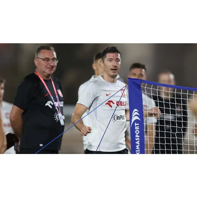 Naturlig gressmatte sett, mann i hvit t-skjorte foran blått og hvitt nett med flere personer i bakgrunnen.