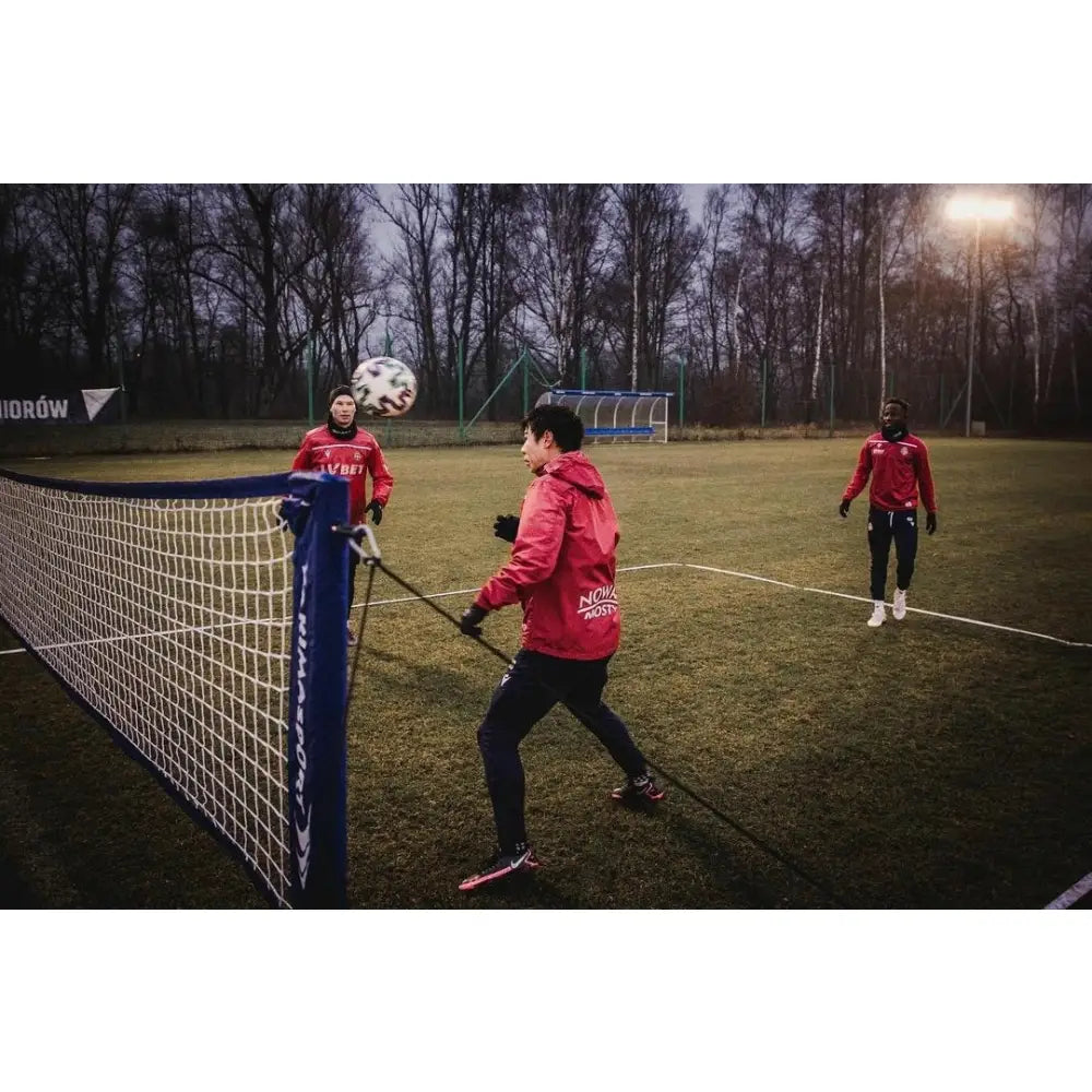 Naturlig gressmatte sett, tre personer spiller fotballtennis utendørs på grønn gressbane, sideperspektiv.