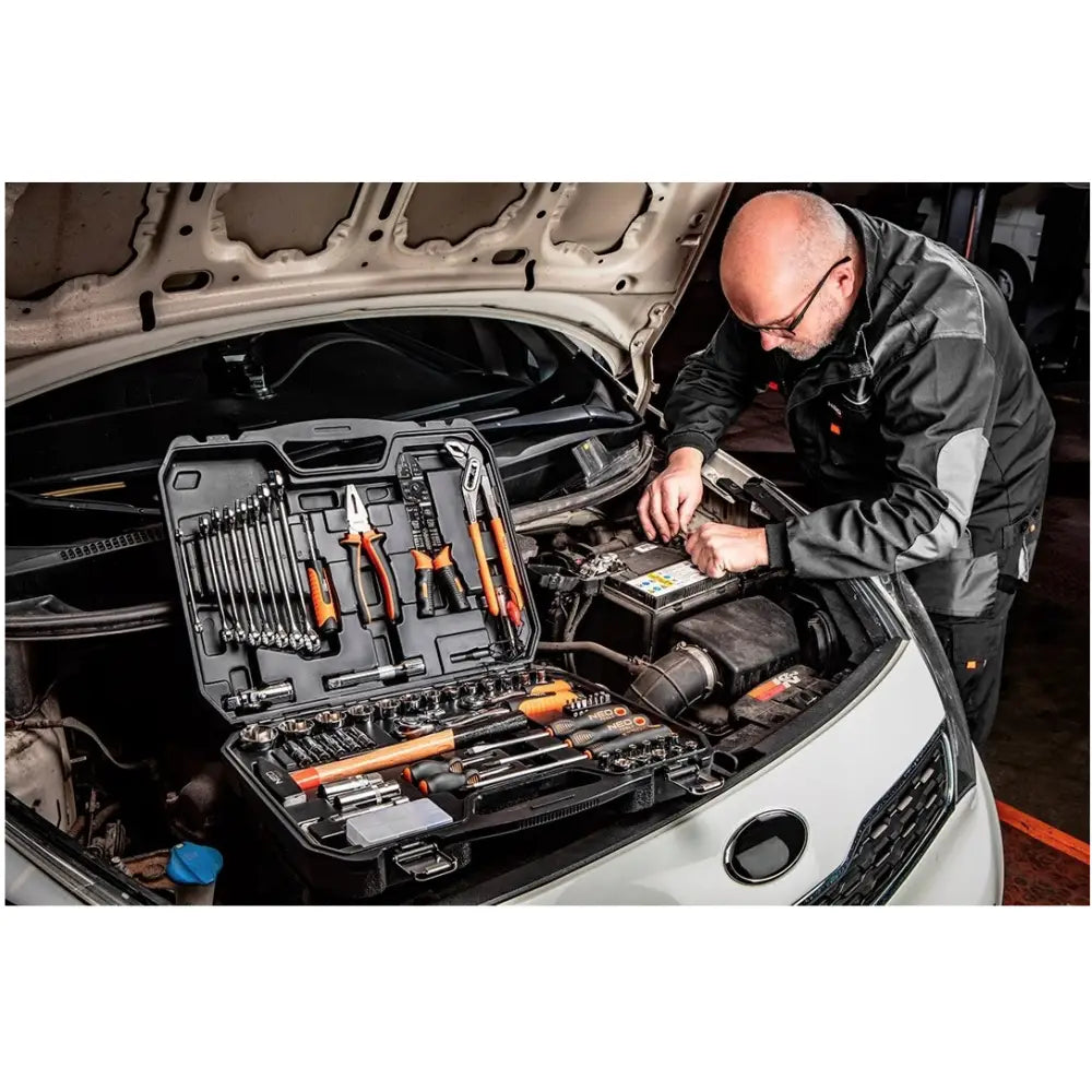 Neo verktøysett med 100 deler, åpen koffert på bilmotor mens en mann utfører reparasjon.