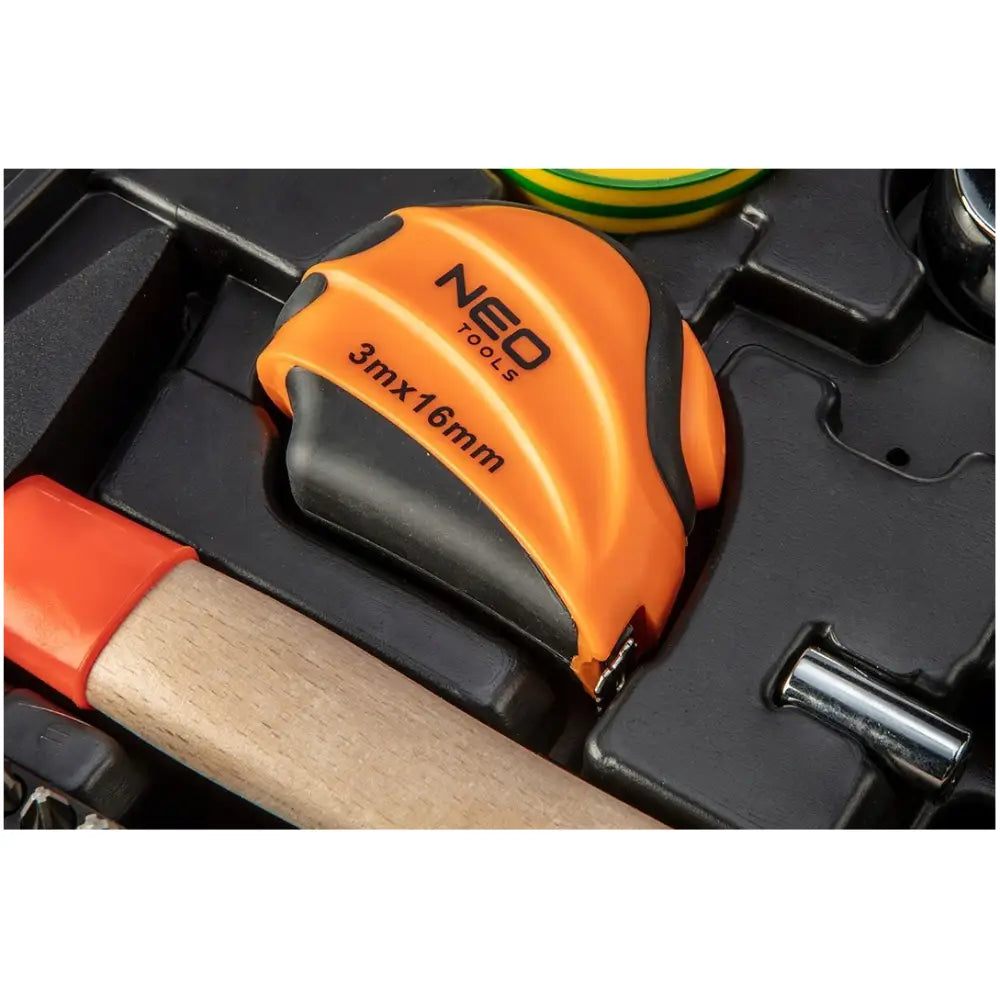 Oransje og svart målebånd i verktøykasse, sett ovenfra med synlig måleenhet og omgivende håndverktøy.