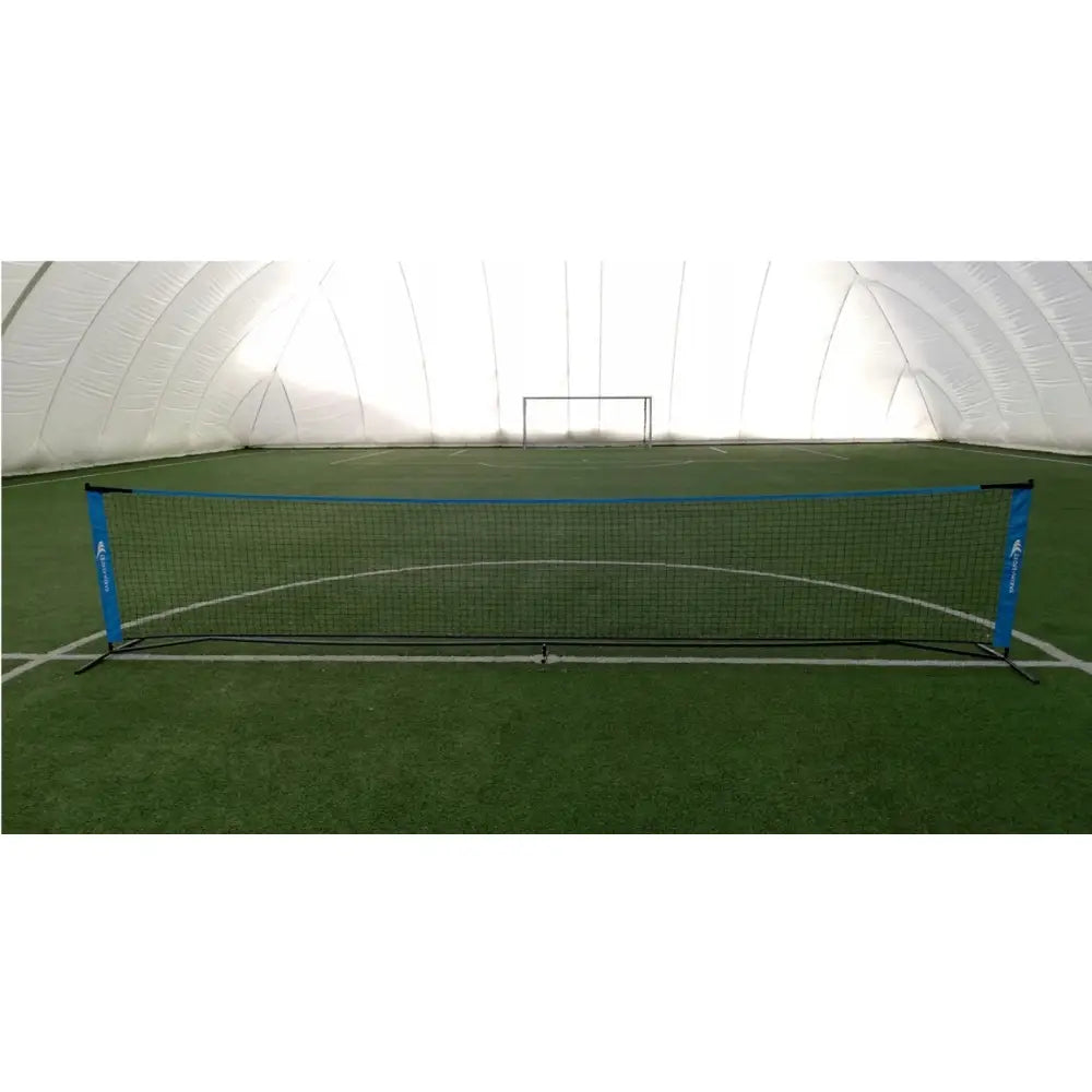Nett for strandvolleyball med kunstgress, svart nett med blå kanter foran grønt innendørs kunstgress.