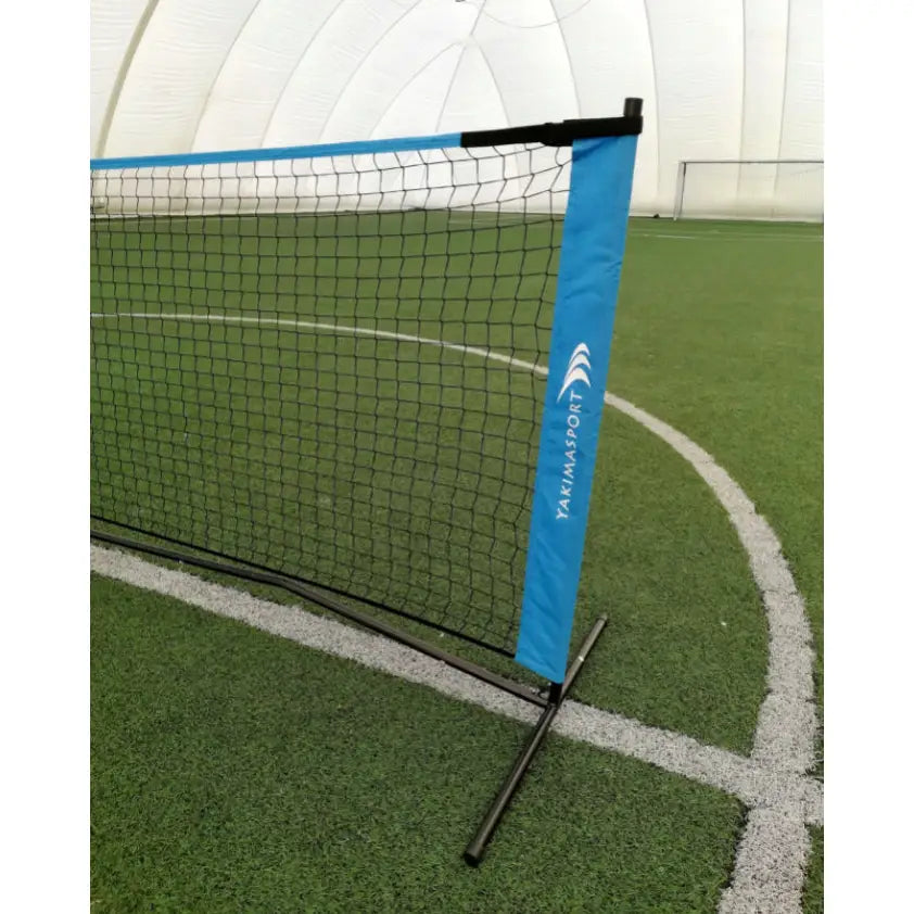 Nett for strandvolleyball med kunstgress, sort nett med blå kant på metallstativ, plassert innendørs.