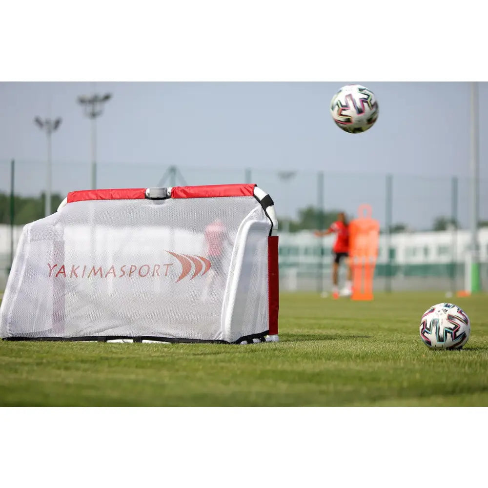 Sammenleggbart ACADEMY fotballmål 120x80 cm, hvitt og rødt nett på gressbane med fotballer bak.