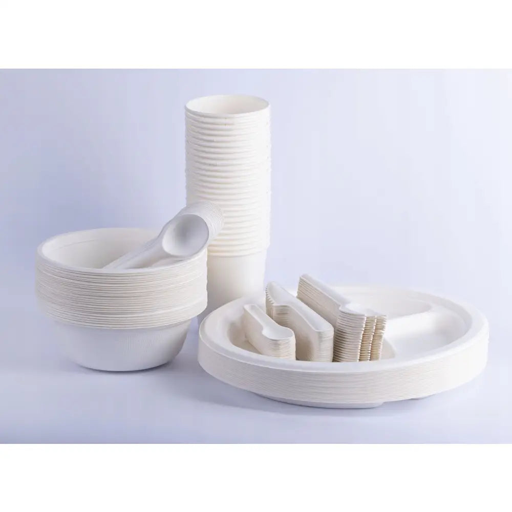 Øko pikniksett med hvite skåler, kopper, tallerkener og bestikk i bioplast, sett skrått forfra.